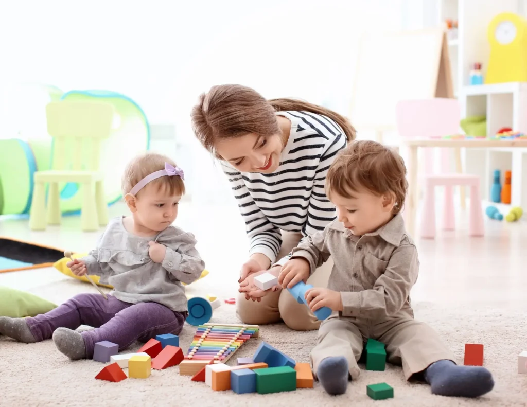 Babysitter playing with two young boys on the ground with wooden blocks