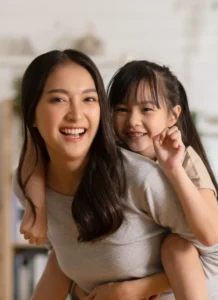 Asian Babysitting and young asian girl with pony tail playing piggy back rides in the kitchen smiling