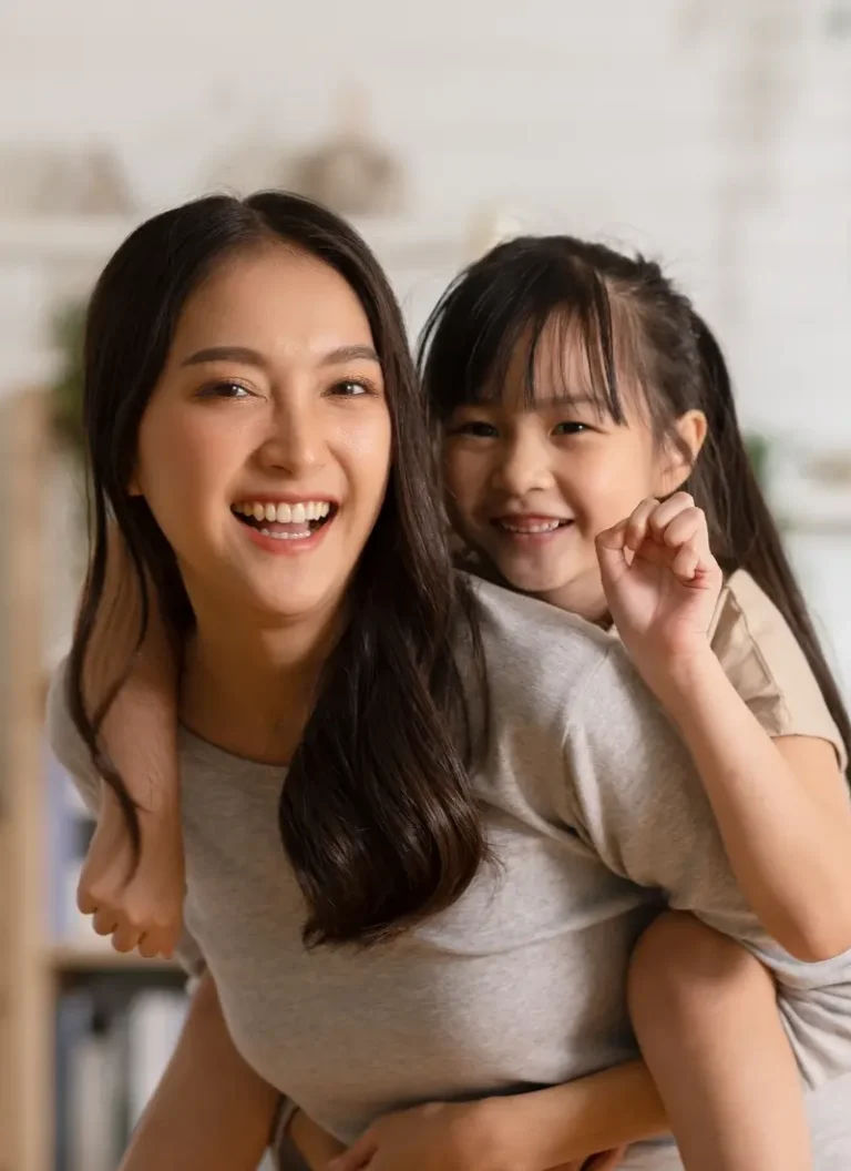 Asian Babysitting and young asian girl with pony tail playing piggy back rides in the kitchen smiling
